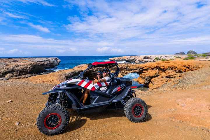 two people in a UTB on dirt next to the ocean
